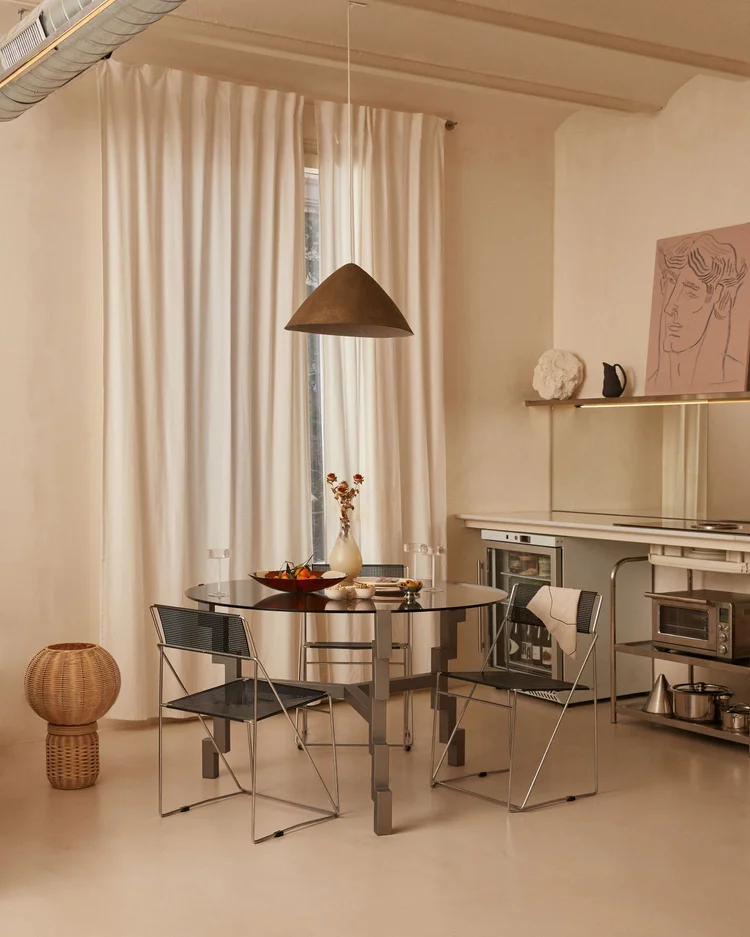 Dining room of Apartment 92 by Santa Living, Isabel Francoy and Anna Enrich, with large light curtains, a round glass table and metal chairs.