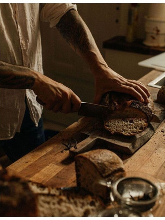 Food photography by Maureen M. Evans for Richard Hart Cookbook — hands slicing rustic bread in warm kitchen light.