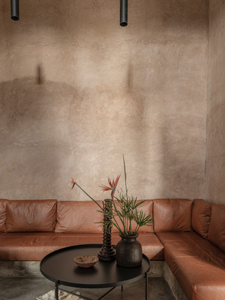 Salon de la Villa D à Marrakech avec canapé d’angle en cuir brun, table basse noire et décor minimaliste sur mur enduit.