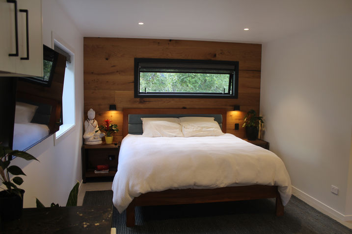 Bed against wood panel feature wall in studio suite by Karaka Park Projects