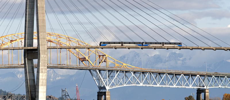 Metro Vancouver bridge and SkyTrain with mountains, representing life in British Columbia