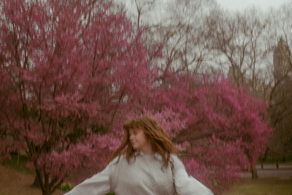 Film‑style portrait of individual twirling amongst the cherry blossoms in Central Park