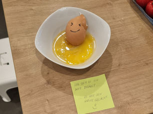 Wichtelstreich mit Humor: Kaputtes Ei mit Smiley-Gesicht und handgeschriebener Nachricht vom Wichtel „Hab dem Ei einen Witz erzählt … es hat sich kaputt gelacht!“