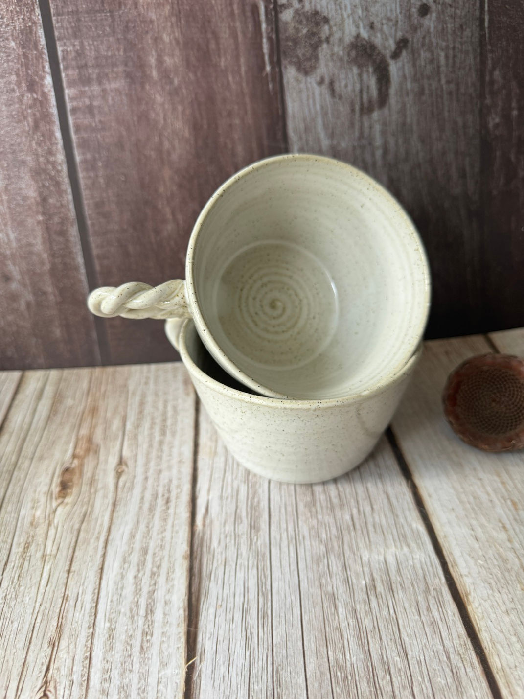 Two white small cappucino mugs with rope handles nestled together on a wooden backdrop