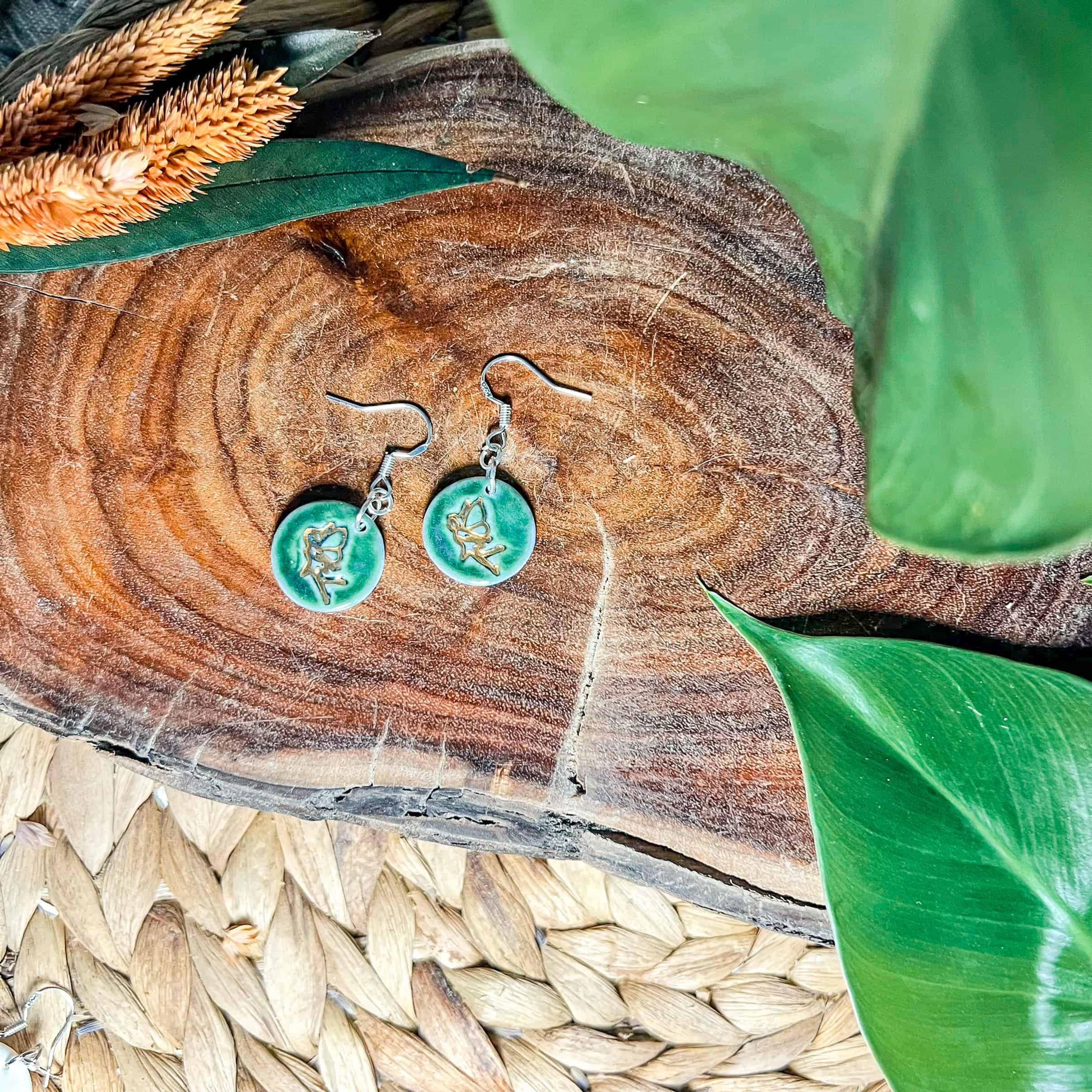 Two circular hook earrings featuring a teal glaze and gold lustre imprint of a fairy
