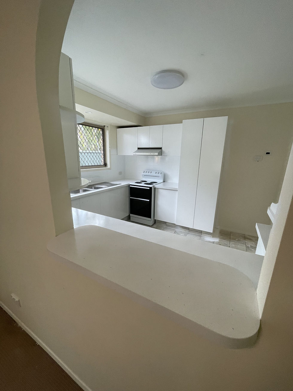 Looking through an arched wall to the resurfaced white kitchen