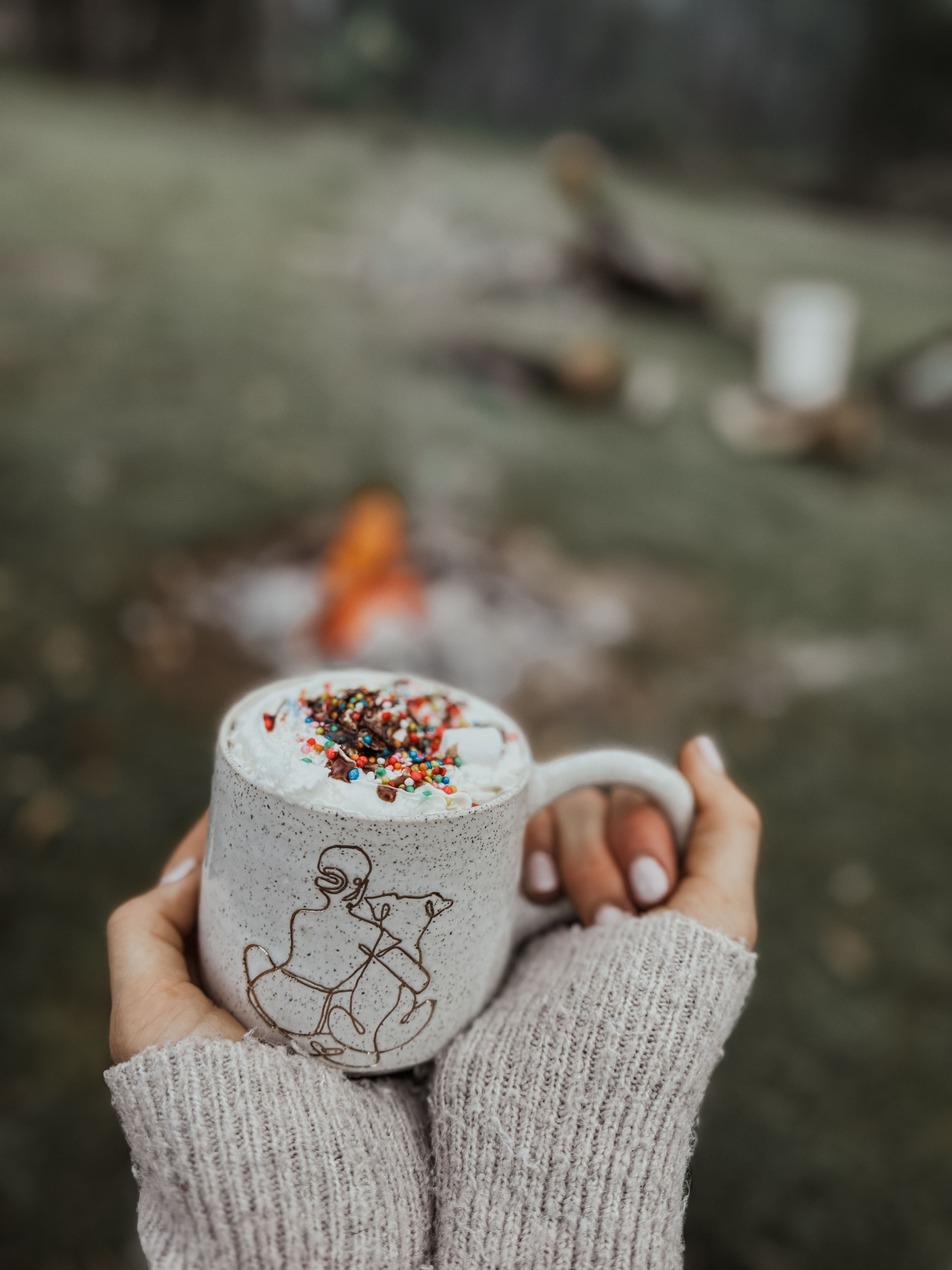 Girl hugging dog mug filled with hot chocolate by a fire