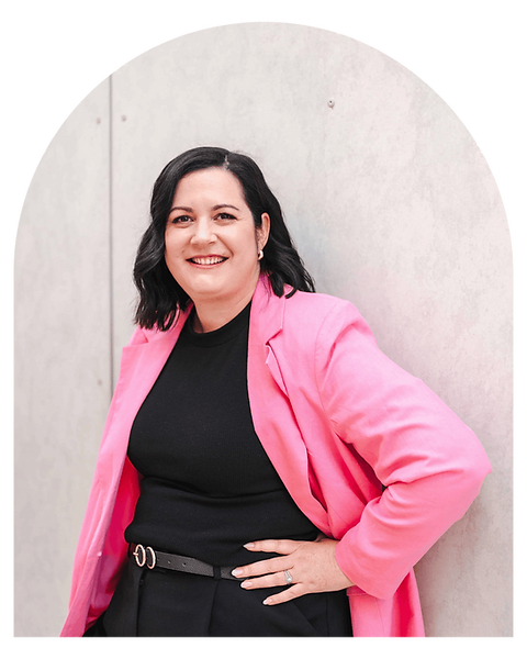 Candice leans against a wall, smiling at camera, arm on hip