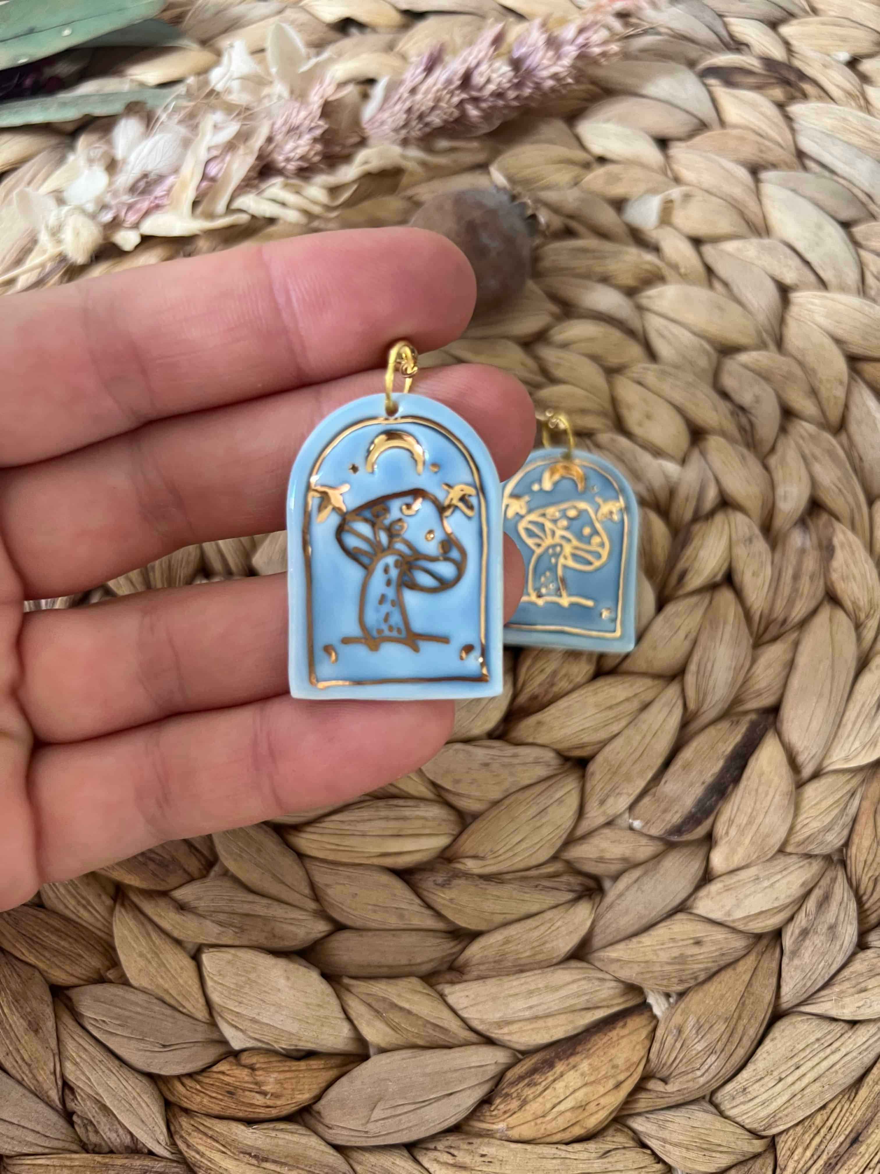 Arch shaped handmade mushroom earrings with gold alloy ball studs. Light blue glaze with gold lustre mushroom, moon and star.