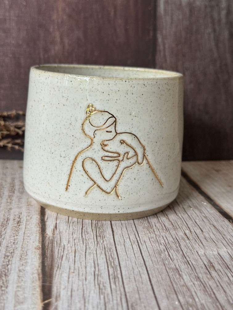 Line drawn woman with bun hugging a dog, in gold detail on a mug