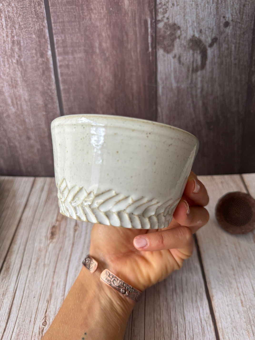 Hand holds a white small teacup with leaf carving at the base