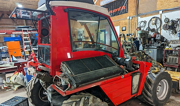 A red tractor that is in a vehicle shop during its restoration process.