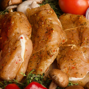 Three stuffed chicken breasts surrounded by fresh vegetables and herbs