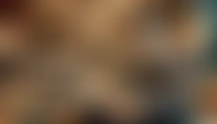 Man in suit using a laptop in a modern lounge with warm lighting. Two men converse in the background. Luxurious, professional atmosphere.