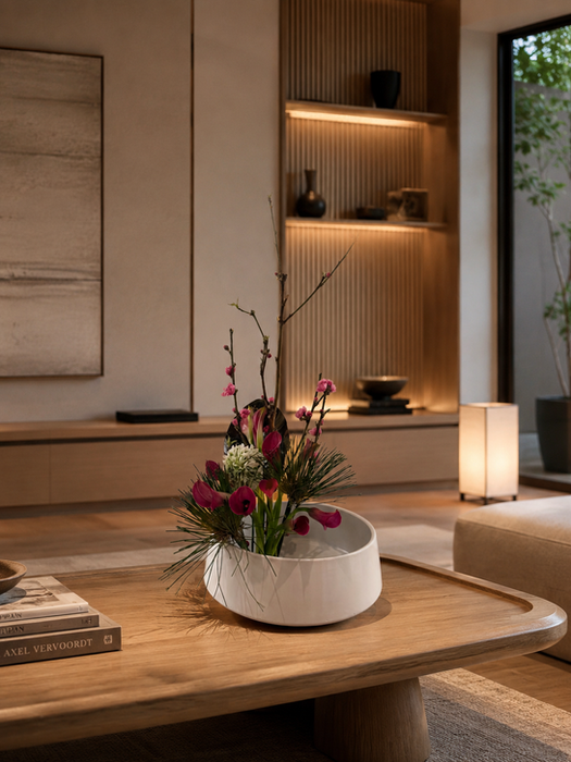 Modern Japanese-inspired floral arrangement with burgundy flowers, greenery, and sculptural branches displayed on a wooden coffee table in a luxurious minimalist living room.