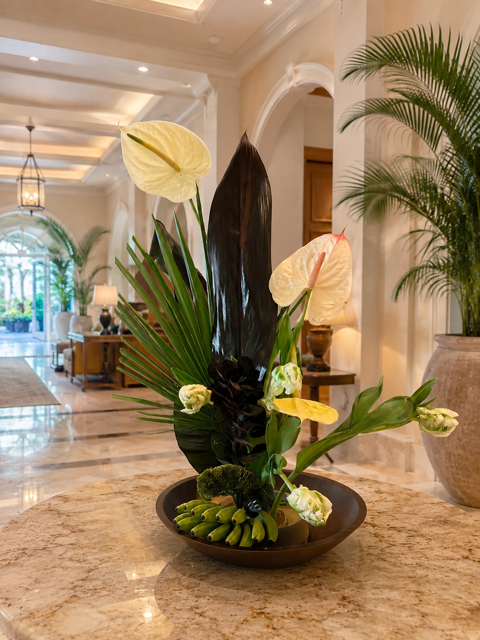 Modern tropical floral arrangement with white anthuriums, dark foliage, and palm leaves displayed on a marble table in a luxury resort-style interior with elegant arches and warm natural lighting.