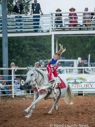 Young girl, Jins, riding a white horse doing a trick spinning around the pommel in front of the crowd at the Hood County Stampede