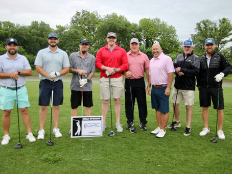 Group of golfers posing before teeing off posing in front of a sponsor sign.
