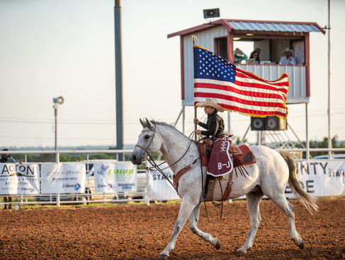 Jet Greene with the American flag riding a horse in the arena at Reunion Grounds in Granbury Texas