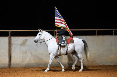 Jet Greene riding his horse with the American flag trotting around a covered arena