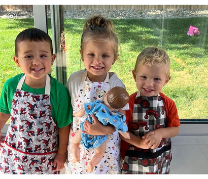 Three toddlers in aprons, holding a baby doll