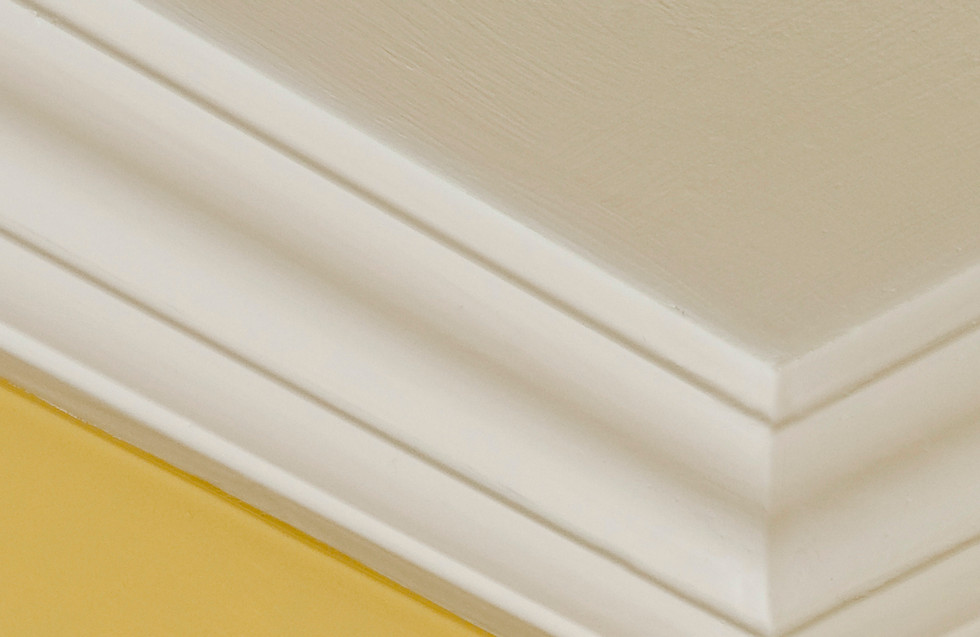Close-up of a yellow wall with white trim, highlighting popcorn ceiling repair details.
