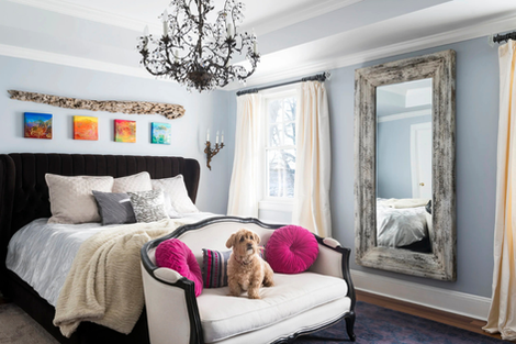 Elegant bedroom with chandelier and dog on sofa.