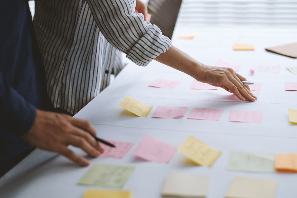 Two people review pink and yellow sticky notes on a white table in a bright meeting room, working collaboratively.