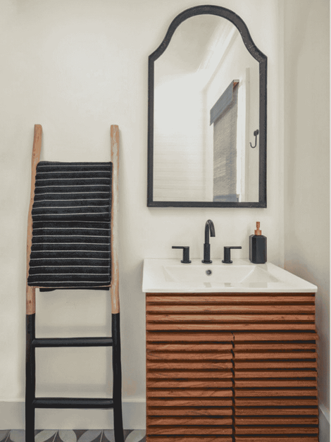small wood vanity with arched black trim mirror