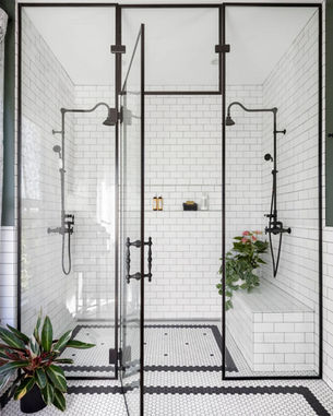 Black grout modern shower with black-framed glass, white subway tiles, and green plants. Hexagonal black and white tile floor adds contrast