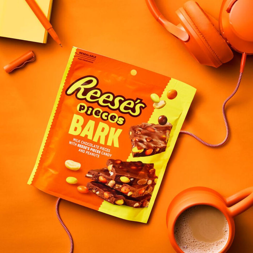 Lifestyle photo of REESE'S PIECES Milk Chocolate Candy Bark bag on orange background with headphones and coffee mug