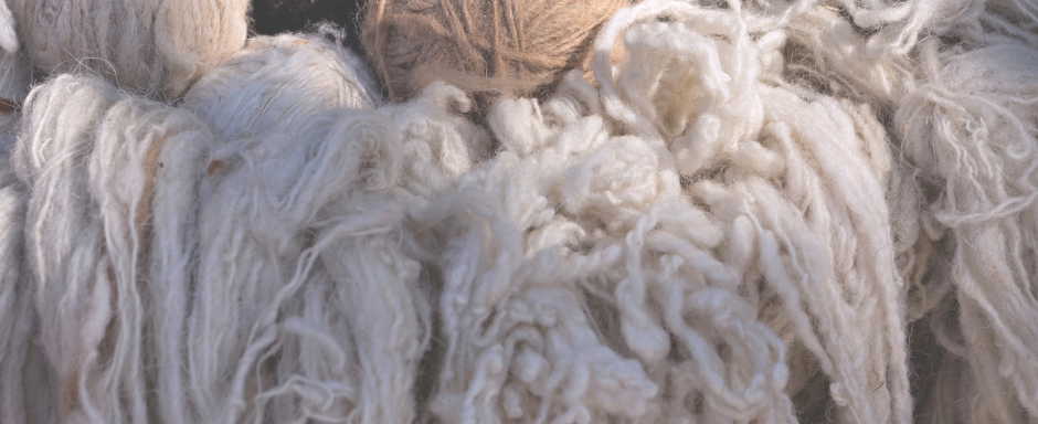 Balls of yellow, brown and white yarn with white handspun wool falling out of a basket