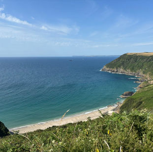 a beautiful sandy bay below the coast path snaking across a cliff top