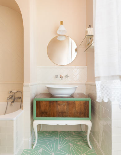 foto con interno di bagno di appartamento. Mobile lavabo vintage con lavabo da appoggio in ceramica. pareti in rosa pallido, boiserie di mattonelle color panna disposte all'inglese. a terra cementine verde salvia con decoro geometrico bianco.