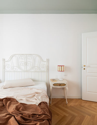 foto con vista su camera da letto di appartamento. soffitto in verde salvia, letto con struttura in ferro battuto verniciato bianco, a terra parquet posato a spina italiana in rovere. porta di ingresso sulla destra.
