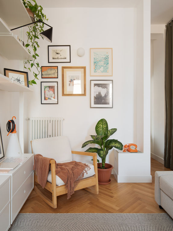vista su interno di appartamento con poltrona in tessuto bianco e legno, a sinistra libreria, sul fondo parete con quadrerie 