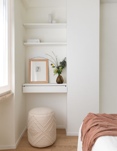 particolare con vista su angolo toletta con pouff in tessuto bianco e falegnameria su misura con ripiano con cassetto e mensole nella parte alta