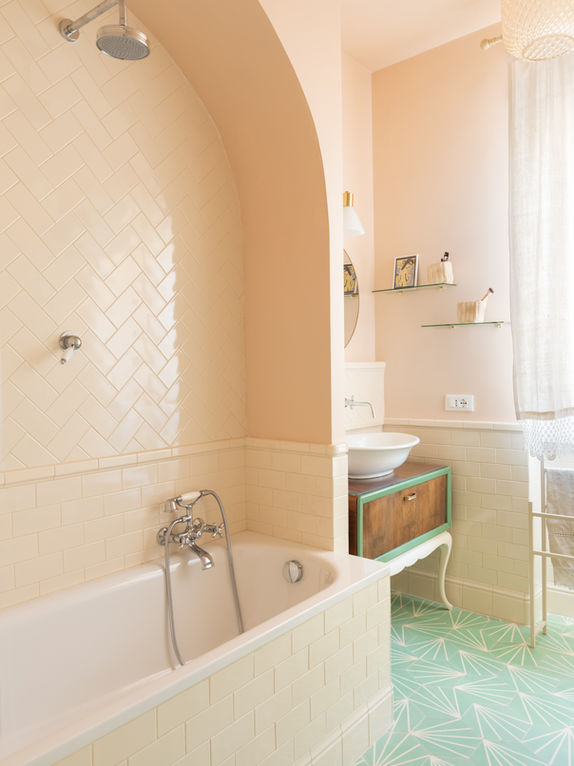 vista su bagno di appartamento con vasca sormontata da nicchia ad arco ad incorniciare lo spazio della doccia. pareti in rosa pallido boiserie di mattonelle color panna disposte all'inglese con torello di rifinitura e basamento in rilievo. a terra cementine decorate verde salvia con disegni geometrici bianchi.