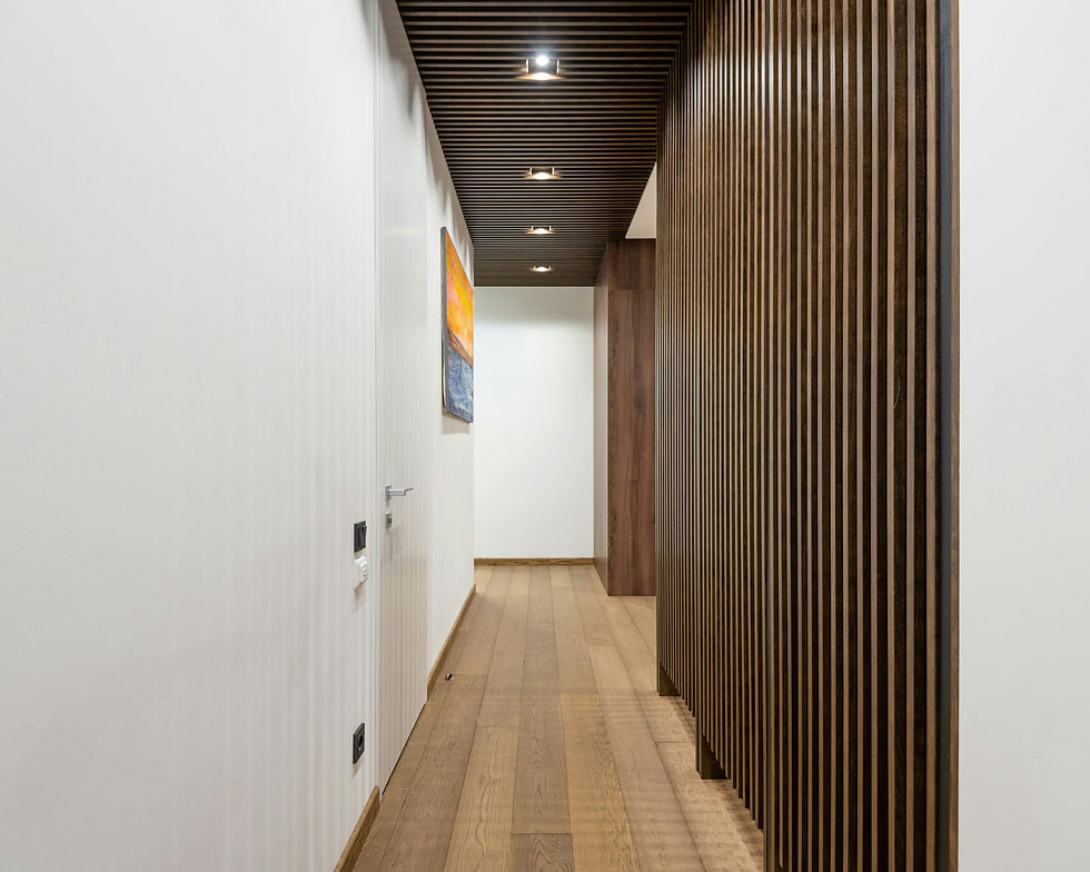 Corridoio moderno con pareti bianche, pavimento in legno, soffitto e divisorio a doghe di legno, faretti a incasso e opere d'arte astratte alle pareti.