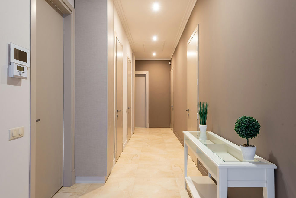 Corridoio luminoso color beige con diverse porte chiuse, termostato a parete e consolle bianca su cui poggiano due piante ornamentali in vaso.