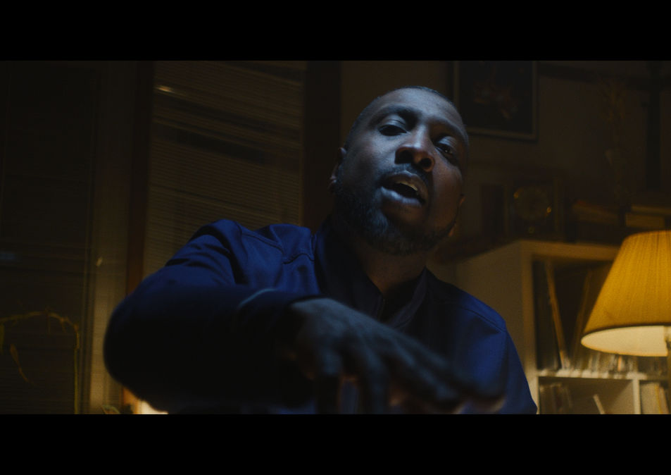 Male performer in a moody, warmly lit room delivering lyrics with emotional intensity during a CrossRoads Productions music video shoot