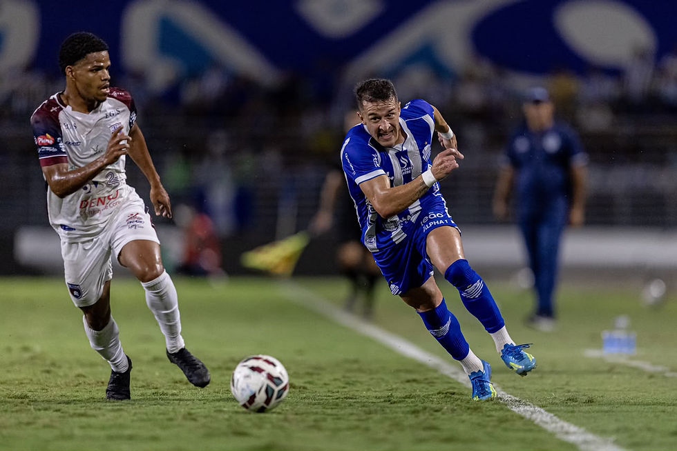 Jogador do CSA, Ronaldo Mendes, vestindo uniforme azul e branco, disputa a bola em velocidade contra jogador do Betim, que veste uniforme branco, durante partida no gramado do Estádio Rei Pelé.