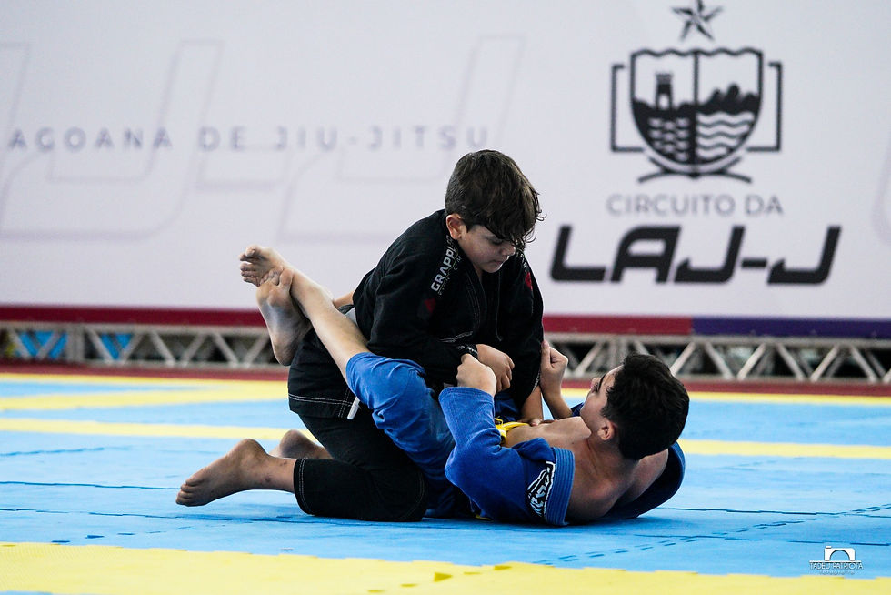 Dois jovens atletas de kimono disputam uma luta de jiu-jitsu durante o Circuito da Liga Alagoana de Jiu-Jitsu; um deles aplica a guarda fechada enquanto o outro busca passagem.