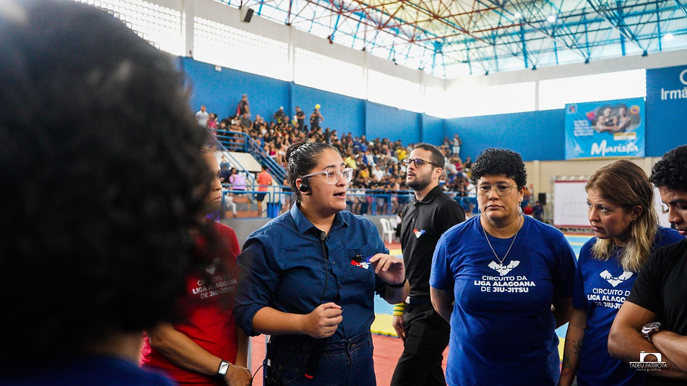 "Organização da Liga Alagoana de Jiu-Jitsu orienta equipe durante competição em ginásio lotado.