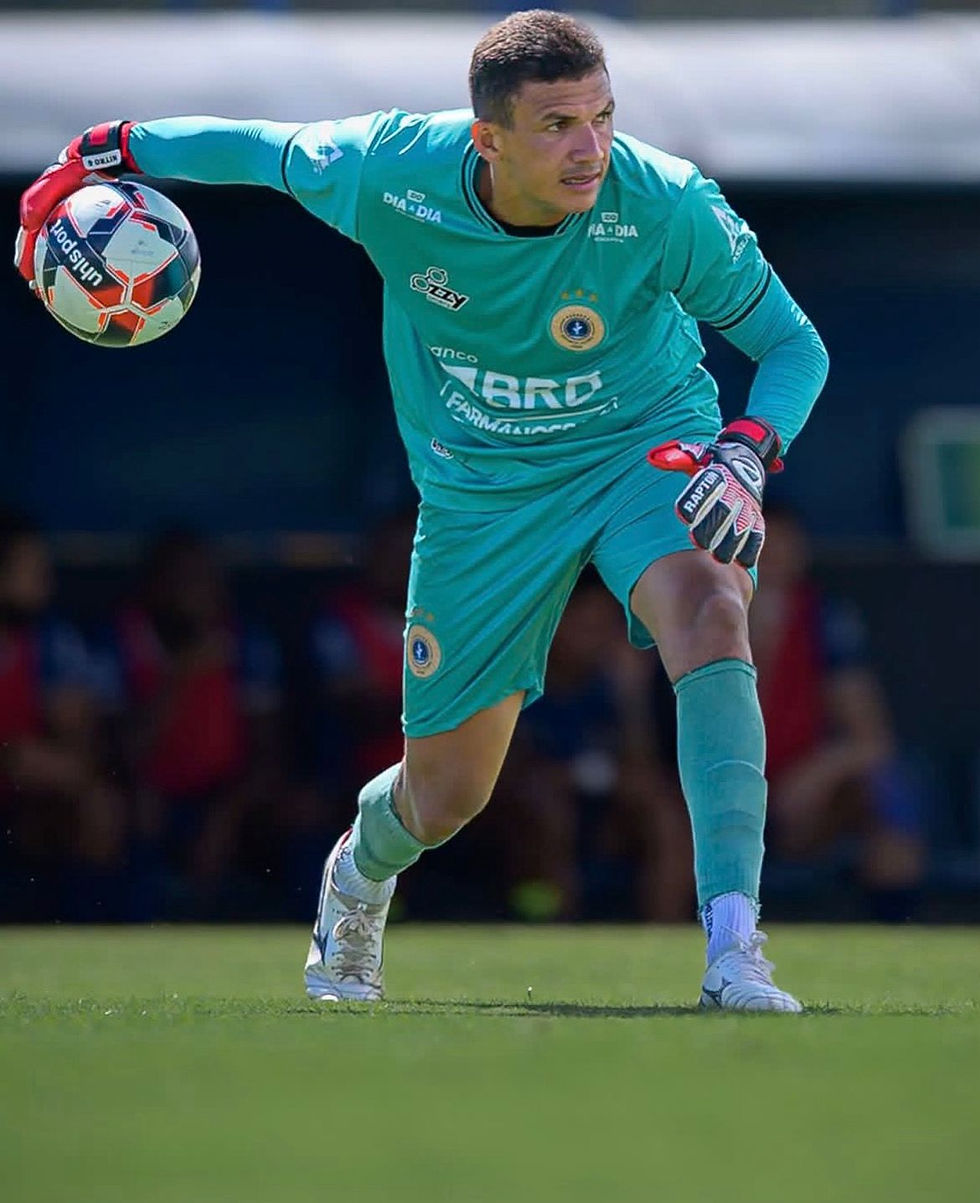 Goleiro do Paranoá em ação, segurando a bola com a mão direita e preparado para lançar, usando uniforme verde e luvas, em campo durante jogo do Candangão.