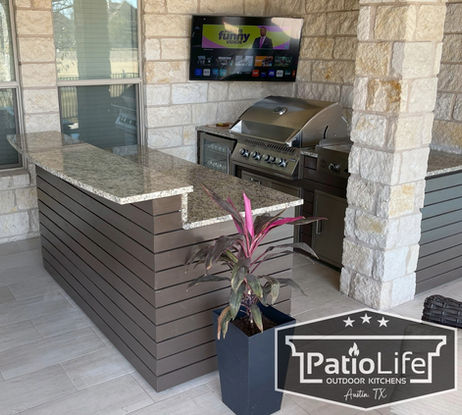 Stunning upgraded patio with custom outdoor kitchen with horizontal slat panel design, granite countertops, and bar seating in Teravista, Round Rock, TX.