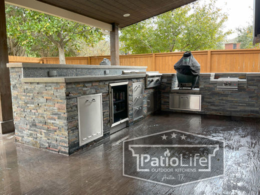 Rustic L-shaped outdoor kitchen with a slate stone veneer finish and a Big Green Egg on a wood-look stamped concrete patio in Teravista, Round Rock, TX.