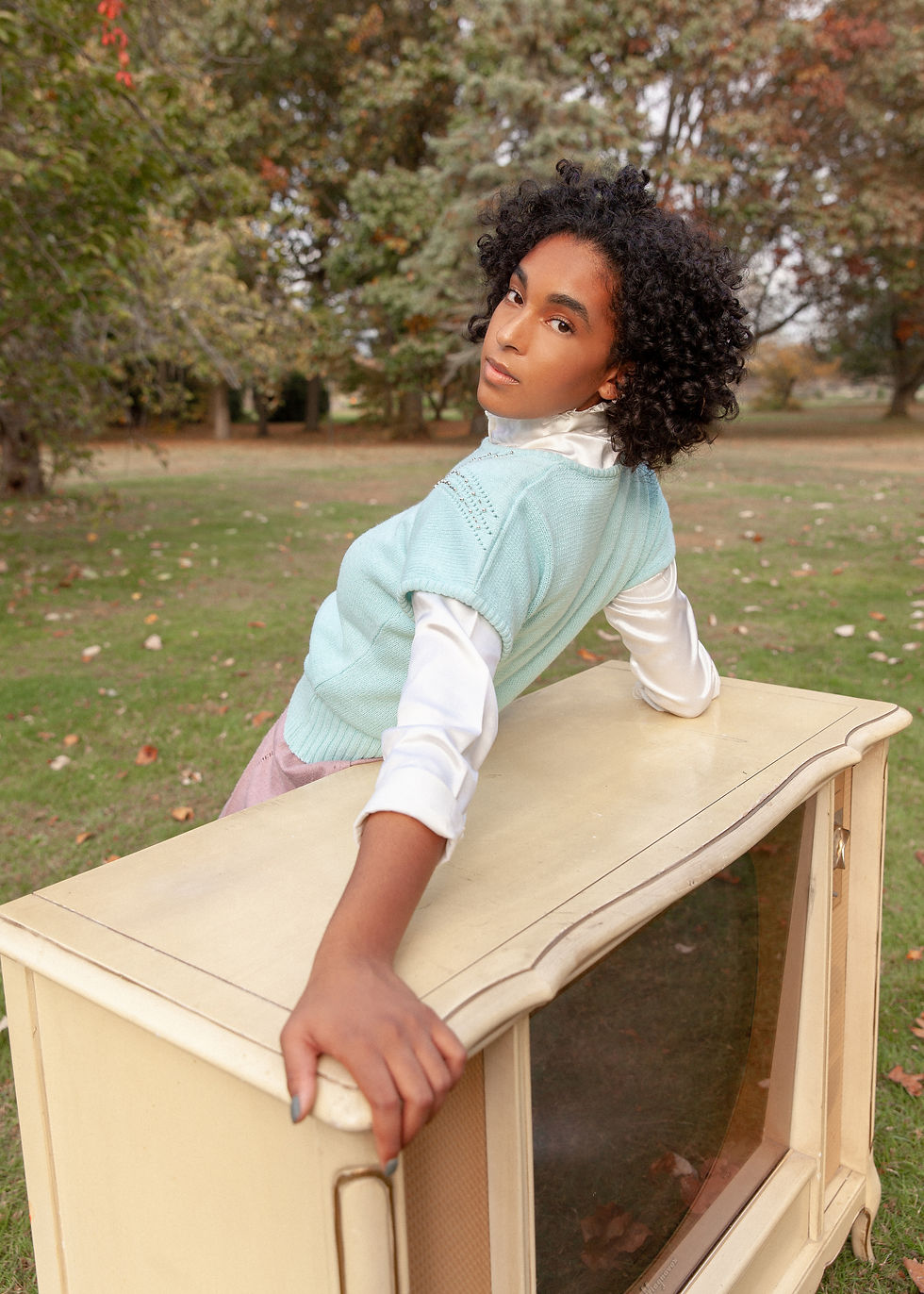 Savannah leaning against an ornate TV in a mint color shirt. Photo taken outdoors with trees in background.