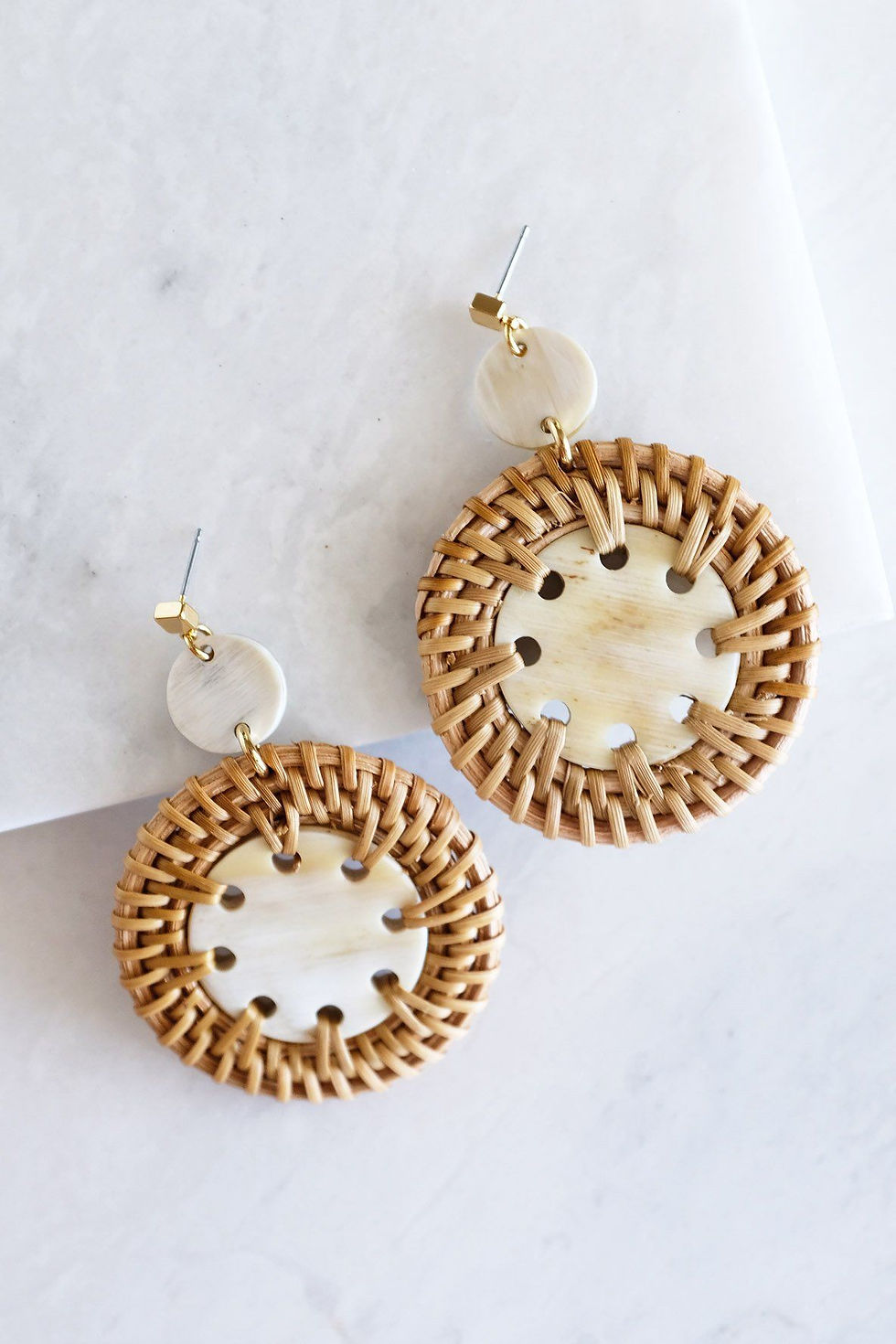 Woven rattan earrings, white accents and Khaam Fefalene, on marble surface.