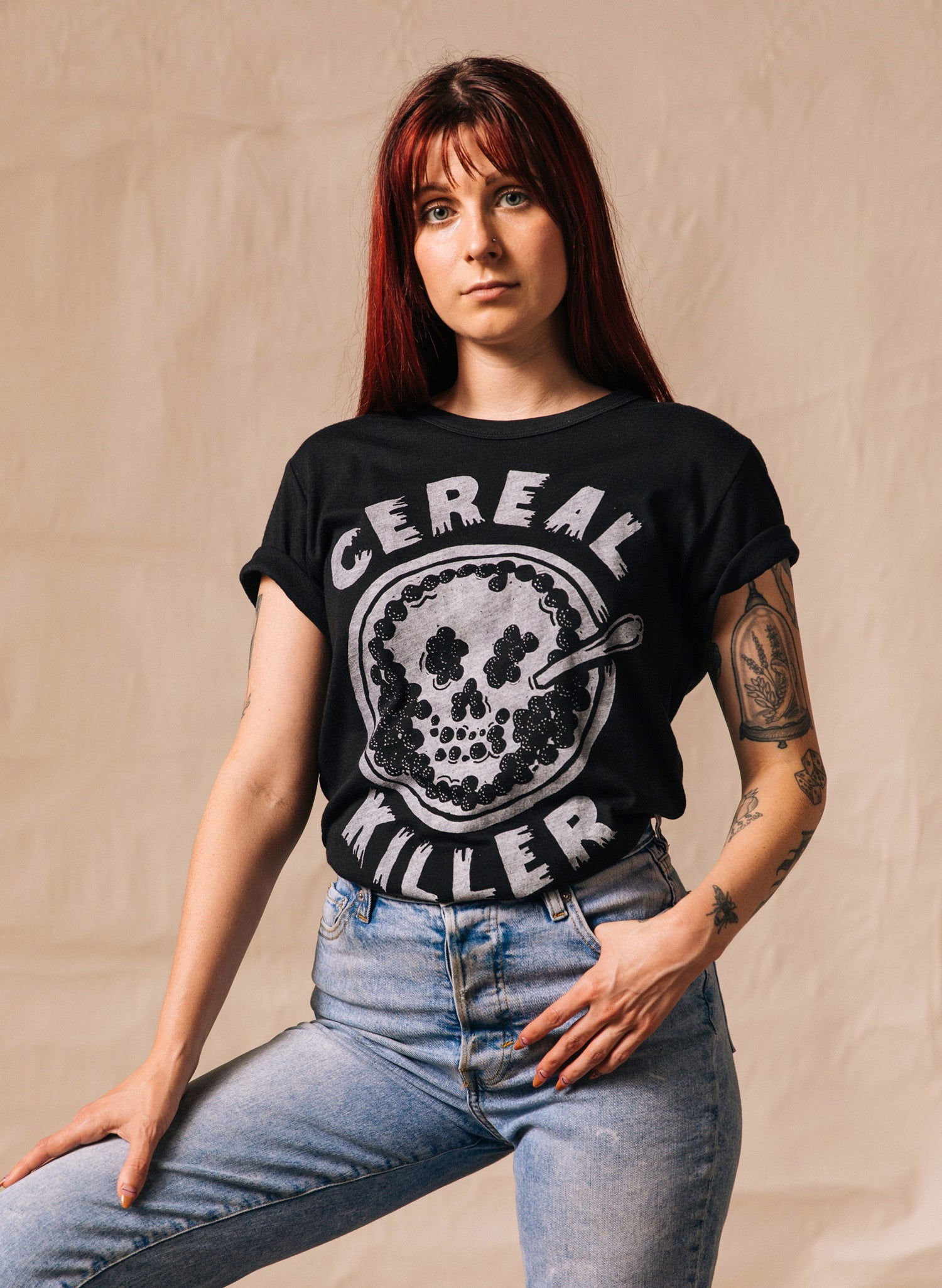 Woman wearing CEREAL KILLER skull t-shirt posing; light background